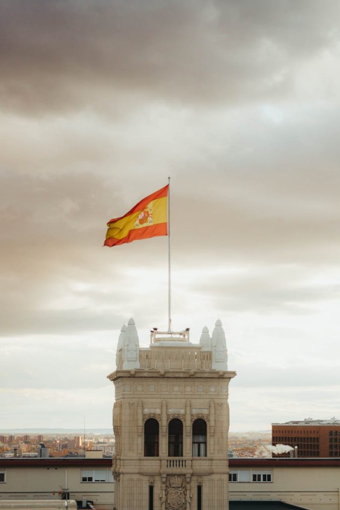 The Spanish flag waves atop an iconic building in Madrid against a dramatic sky.